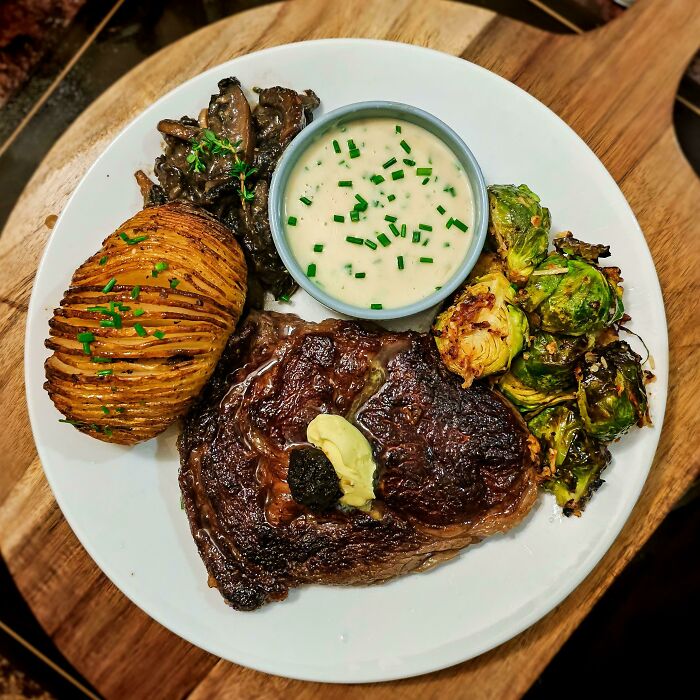 Perfectly cooked steak with seasoned potatoes, sautéed mushrooms, roasted Brussels sprouts, and creamy sauce garnished with chives.