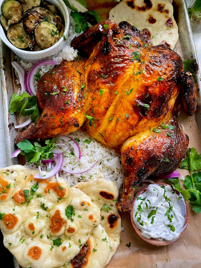 Roasted chicken served with naan, rice, grilled zucchini, and a side of herb sauce, showcasing perfection in food presentation.