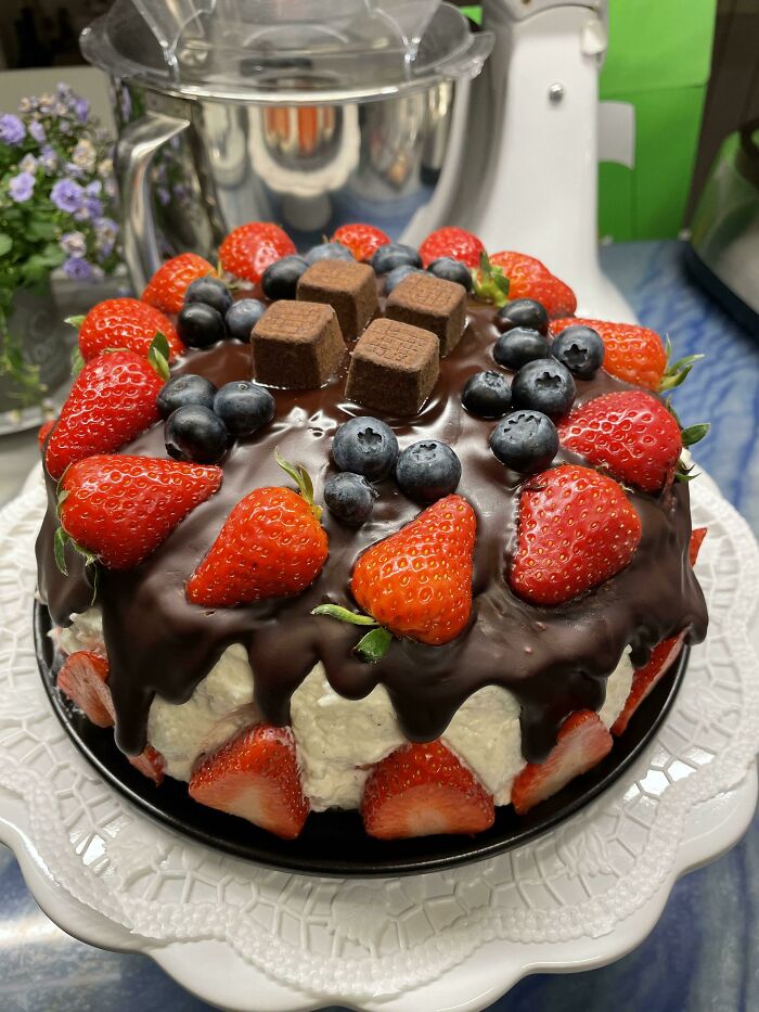 Chocolate-covered cake topped with fresh strawberries, blueberries, and chocolate pieces displaying perfection in food.