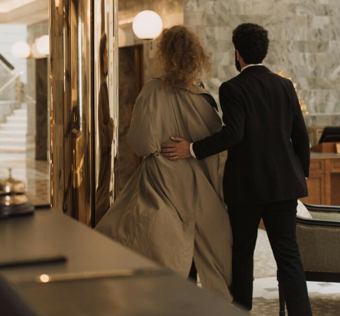 A luxury resort employee in a suit guiding a guest in a trench coat through the marble lobby interior.
