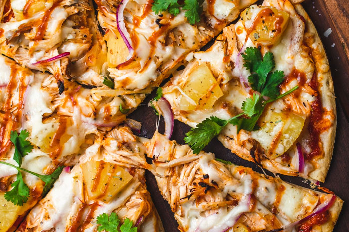 Close-up of a cheesy chicken and pineapple pizza with fresh herbs and barbecue sauce, illustrating unfiltered food opinions.