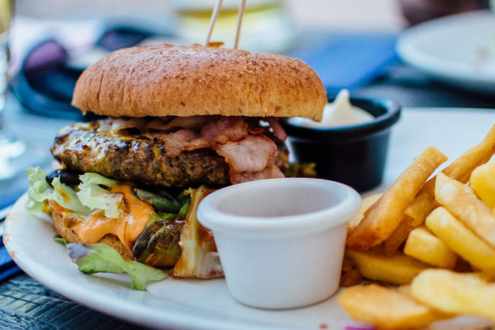 Close-up of a bacon cheeseburger with lettuce and dipping sauces served with fries, illustrating food opinions on crunchy vinegar.