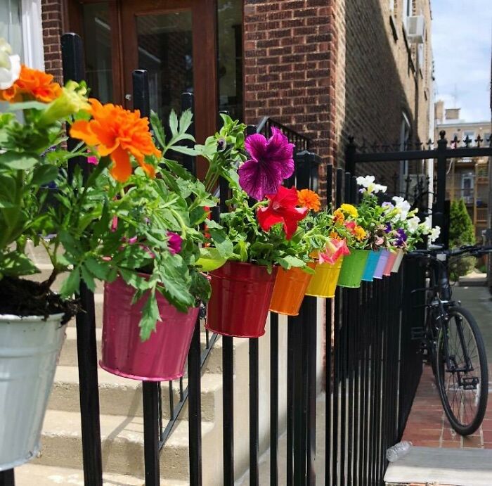 Colorful low-effort garden finds with potted flowers hanging on a black metal fence along urban steps and a brick building.