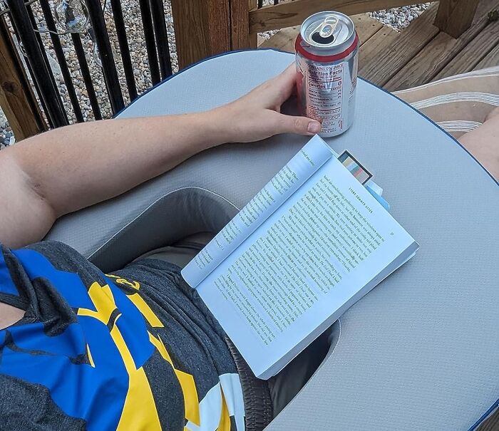 Person reading a book and holding a canned drink while relaxing on an outdoor chair with executive order finds.