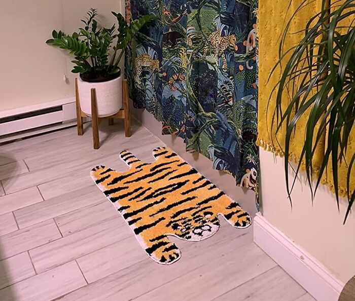 Tiger-shaped rug on wooden floor next to potted plants and colorful curtain.