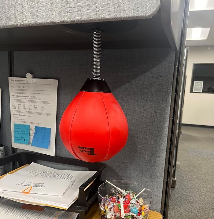 Red Tech Tools punching bag mounted under office desk among papers and candy bowl, a quirky Amazon find.