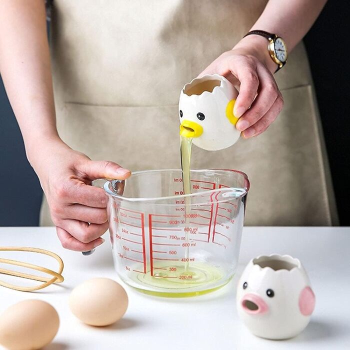 Person using weird kitchen item: chick-shaped egg separator over a measuring cup.