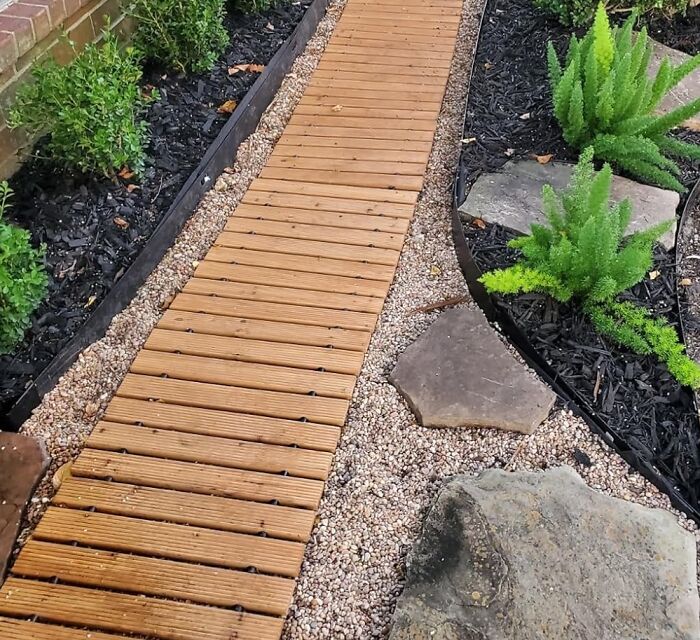 Wooden garden path bordered by low-maintenance plants and small rocks for easy garden landscaping ideas.
