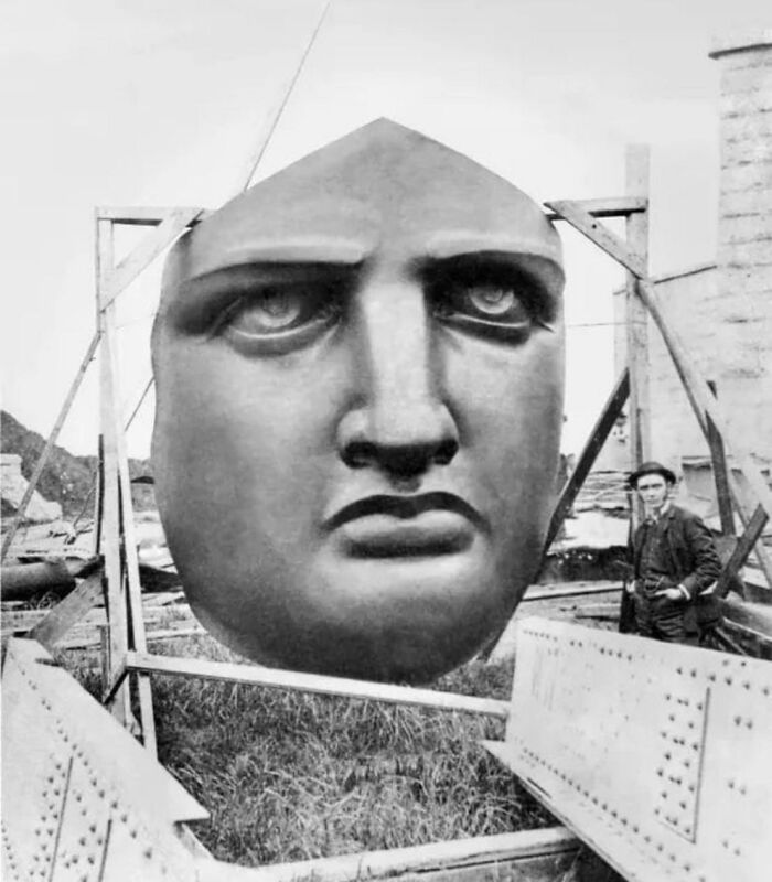 Giant face sculpture of a famous landmark, with a worker beside it, providing a new perspective on its construction.