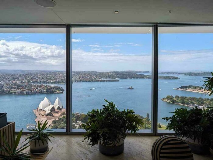View of Sydney Opera House and harbor through large window, offering a new perspective on famous places.