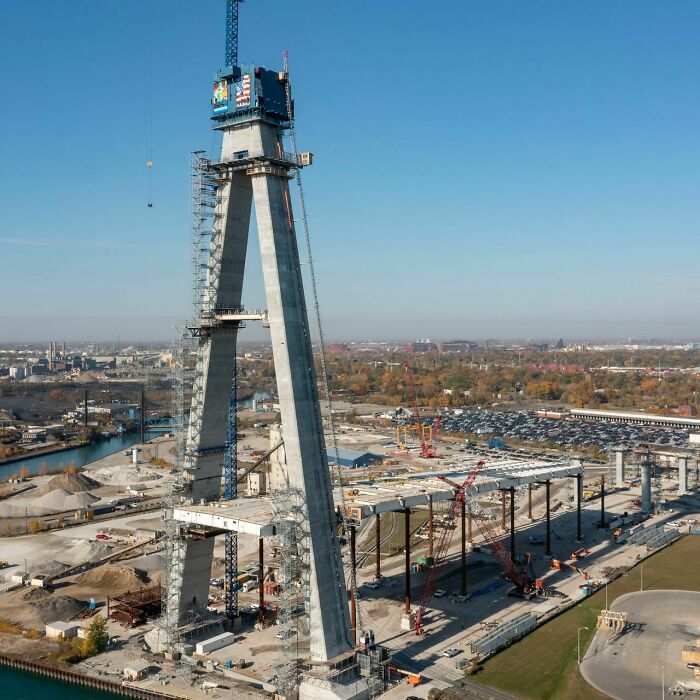 Aerial view of brilliant infrastructure construction site featuring a tall concrete tower and bridge framework under clear blue sky.