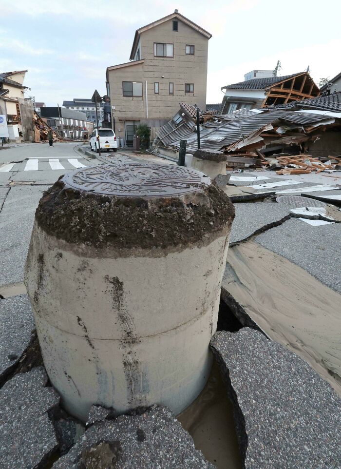 Exposed infrastructure pipe emerging through c*****d street with damaged buildings in the background after disaster.