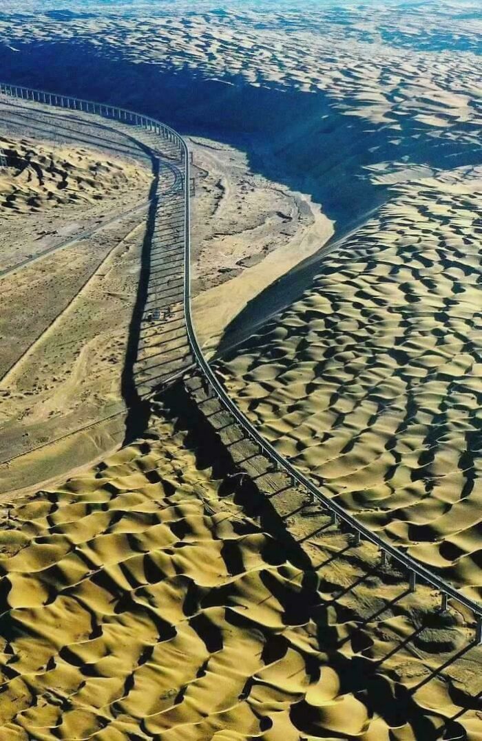 Aerial view of brilliant infrastructure railway curving through vast desert landscape with sand dunes.