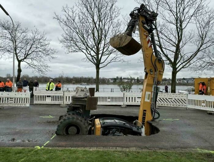Excavator sunk in road, surrounded by onlookers, illustrating an expensive unfortunate incident.