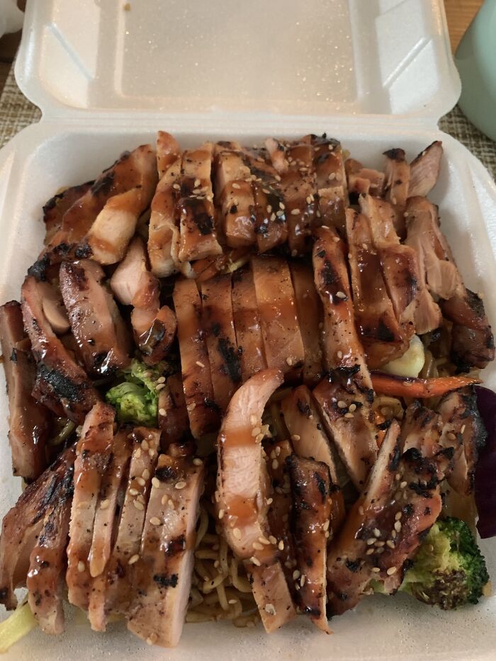 Generous portion of sliced teriyaki chicken on noodles in takeout box, beautifully complying with extra food request.