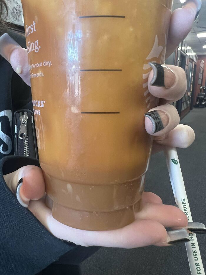 A large iced coffee with layers held by a person with black nail art, showcasing extra caramel.