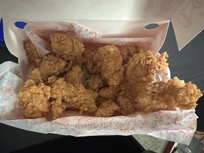 Box of crispy fried chicken placed on wax paper, showcasing generous food service compliance with customer requests.