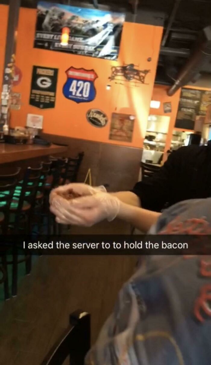 Food service worker holding bacon with gloved hands, complying with customer's request in a restaurant setting.
