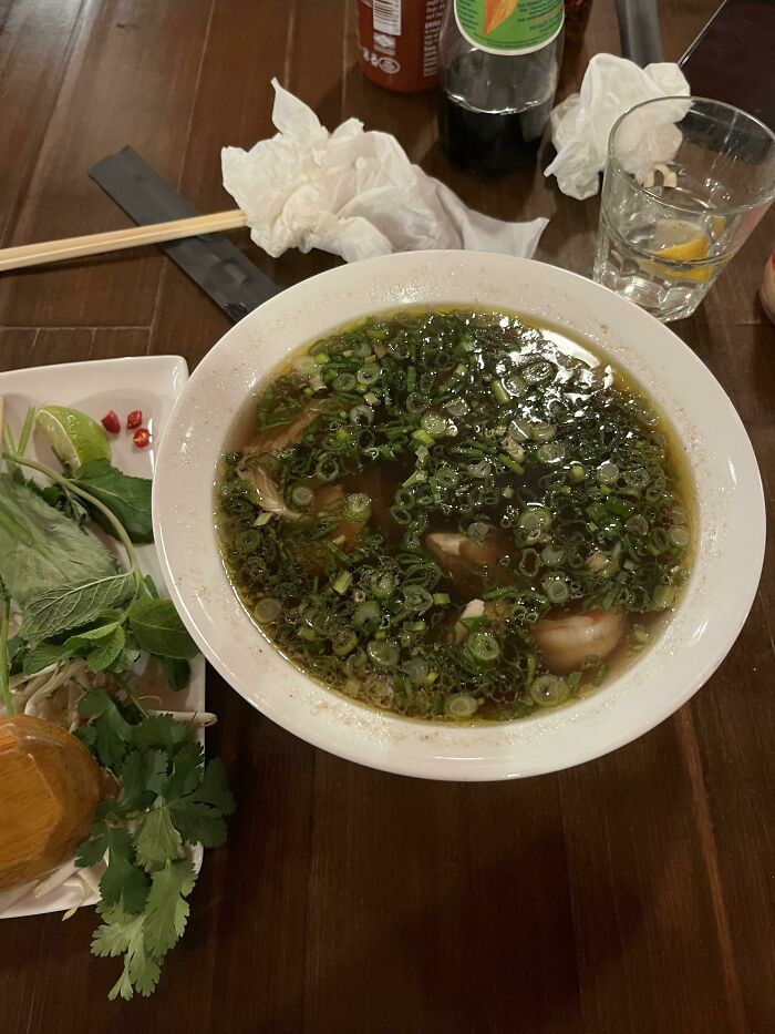 Bowl of soup generously topped with green onions, showcasing food service workers fulfilling customers' requests for extra.