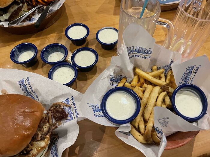 Food service worker fulfills request with extra ranch cups beside burger and fries.
