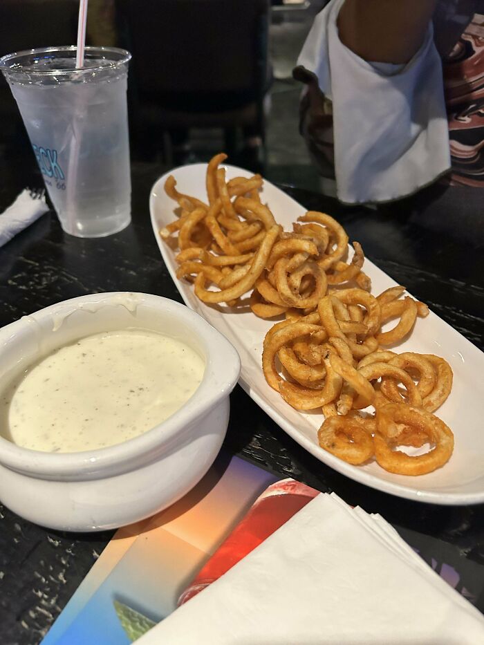 Curly fries with extra portion, served with dip and a drink, highlighting customer's request fulfilled by food service workers.