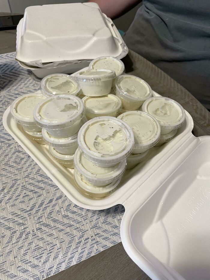 Extra sauce request fulfilled with multiple small containers placed in open takeout boxes on a table.