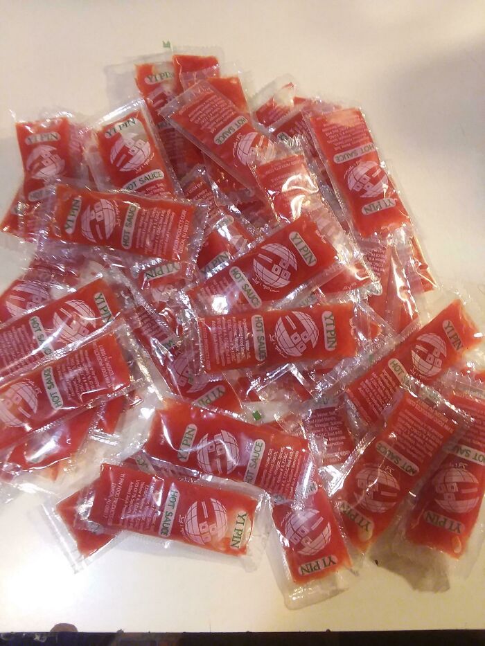 Many packets of red hot sauce on a surface, showcasing food service workers' compliance with requests for extra condiments.