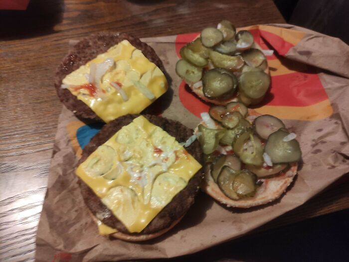 Burger with extra pickles and cheese on a wrapper, showcasing a customer's request fulfilled by food service workers.