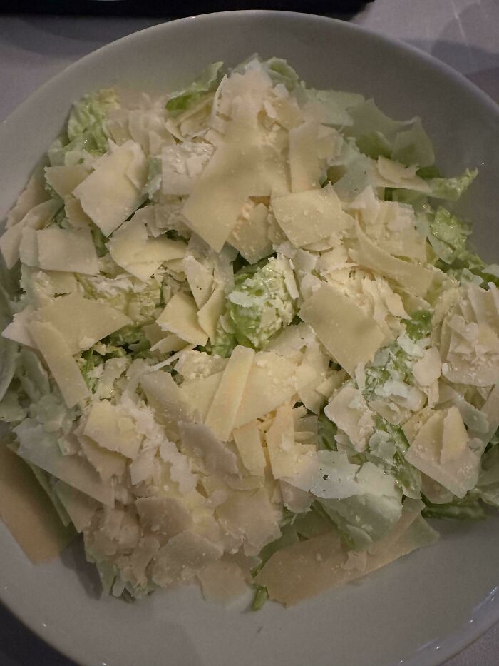 Extra cheese topping generously covering a fresh Caesar salad in a bowl.