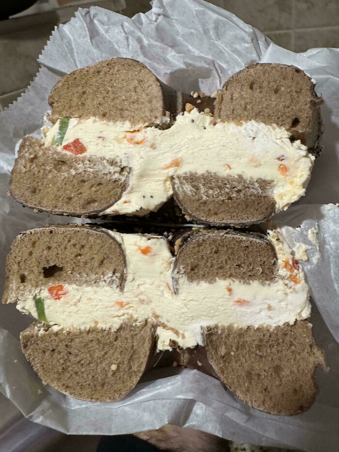 A bagel loaded with generous cream cheese, showcasing food service workers fulfilling extra requests.