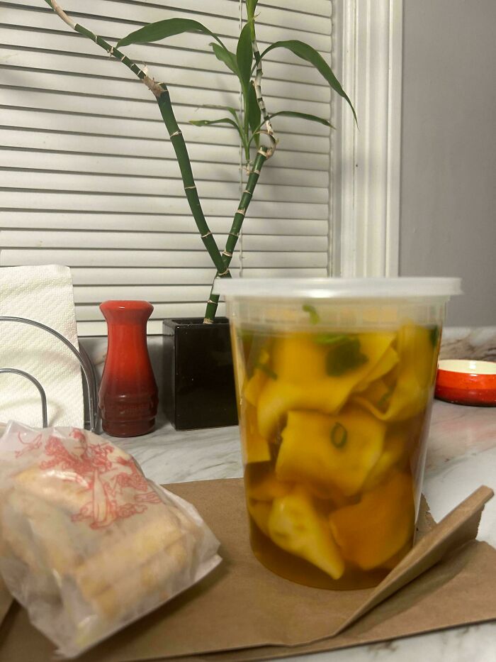 Container of wanton soup with extra dumplings on table, showcasing food service workers fulfilling customer requests.
