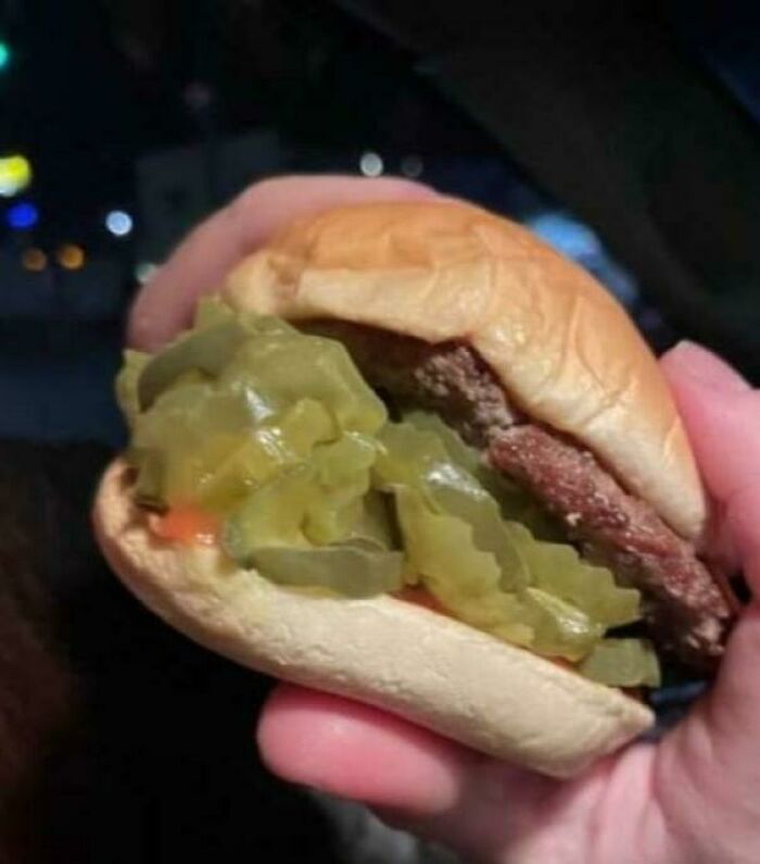 Person holding a burger loaded with extra pickles, displaying generous compliance with a customer's food request.