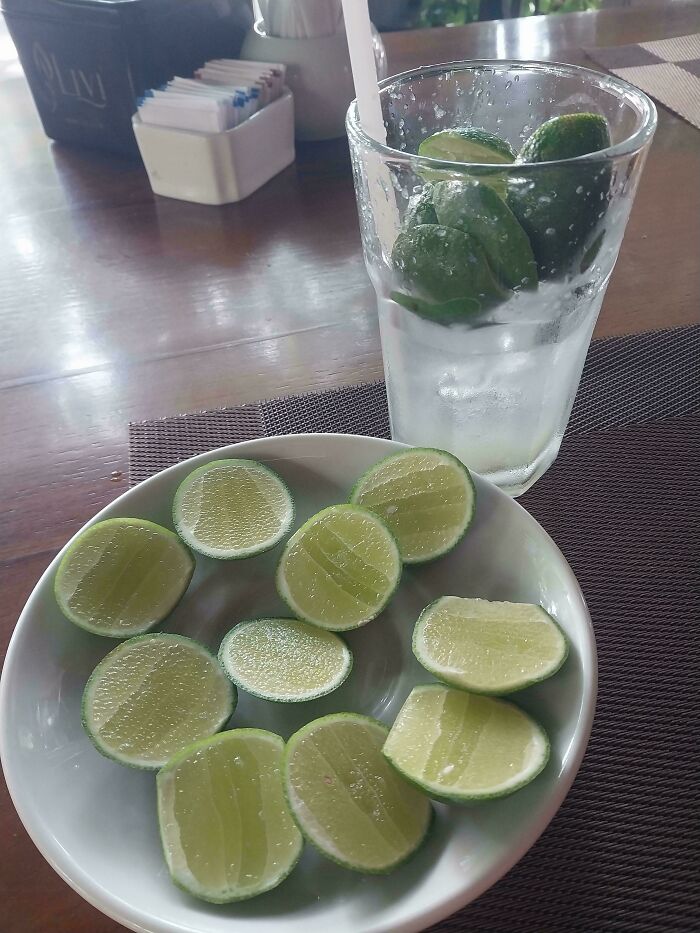 Extra lime slices on a plate and in a glass of water, showcasing food service workers fulfilling customer requests.