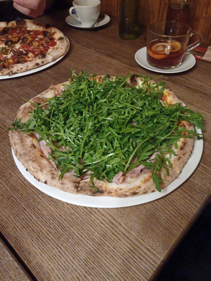 Pizza topped with an extra amount of arugula, satisfying a customer's food request.