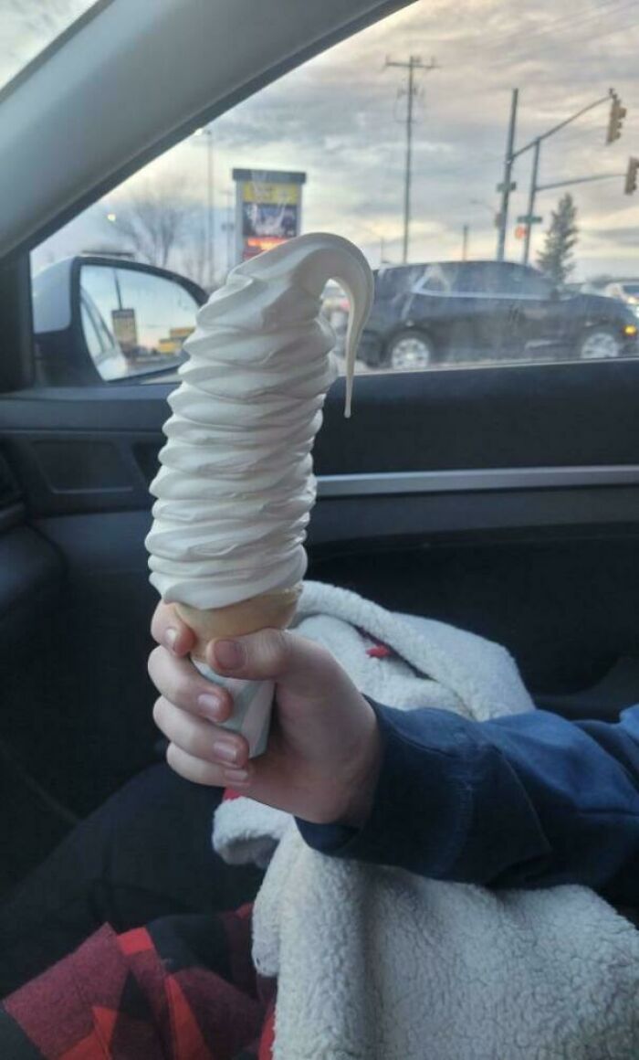 Extra large ice cream cone held in a person's hand inside a car, demonstrating food service compliance with requests.