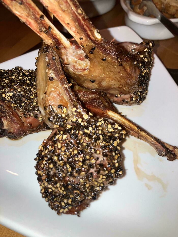Three racks of lamb with a generous pepper crust on a white plate, showcasing compliance with extra seasoning requests.