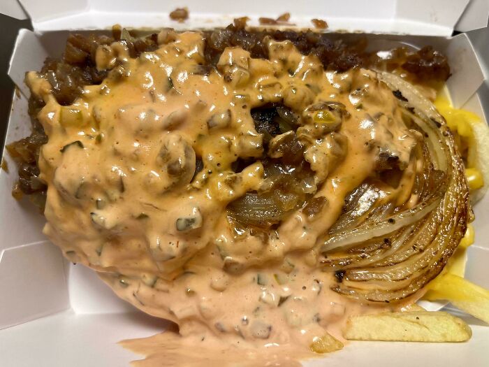 Extra toppings on fries with creamy sauce and caramelized onions in a takeout box, showcasing delicious food service compliance.