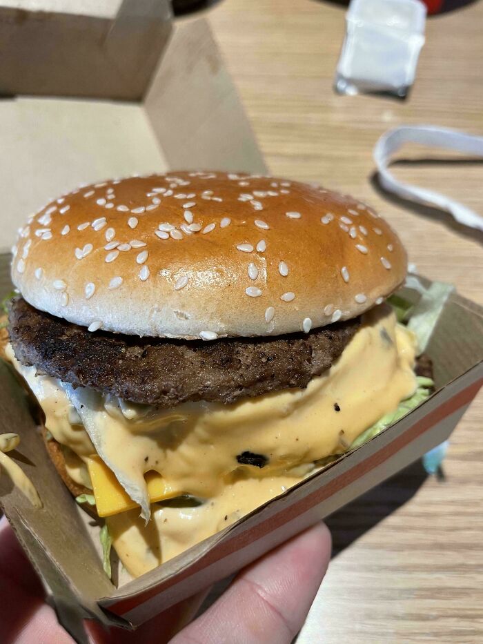 Burger with extra melted cheese requested by customer, served in a cardboard box.