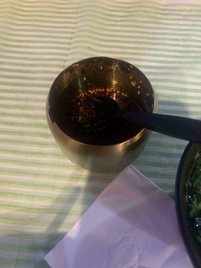Extra sauce served in a small bowl with a spoon on a striped tablecloth.