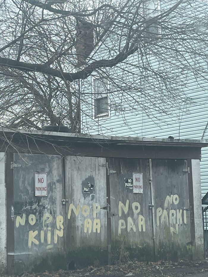 Sign fail with poorly painted "No Parking" message on a weathered garage, displaying confusing text.