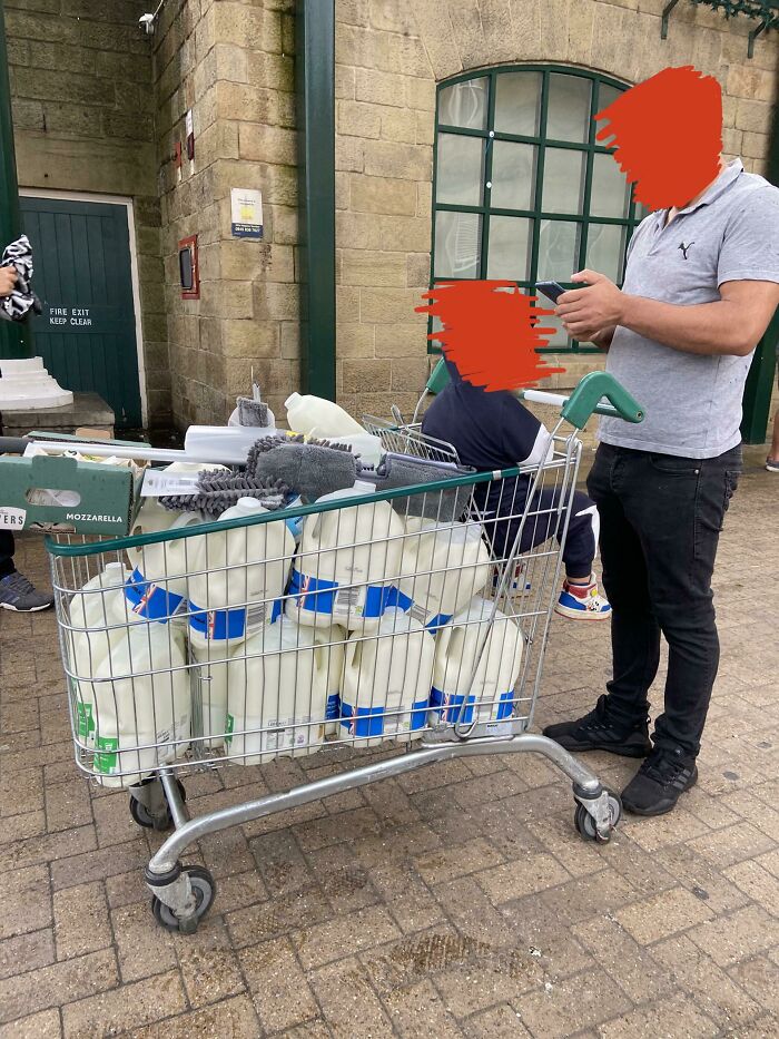 Shopping cart filled with milk jugs in a UK setting, with a stone building in the background, embodying British humor.