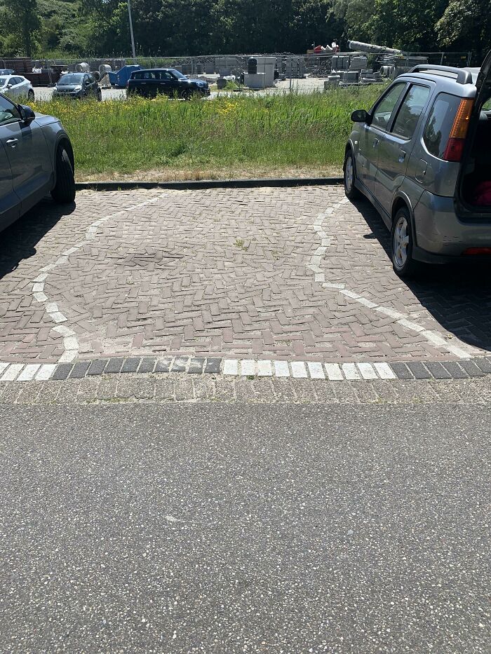 Parking fail with mismatched bricks in a parking space, two cars on either side.