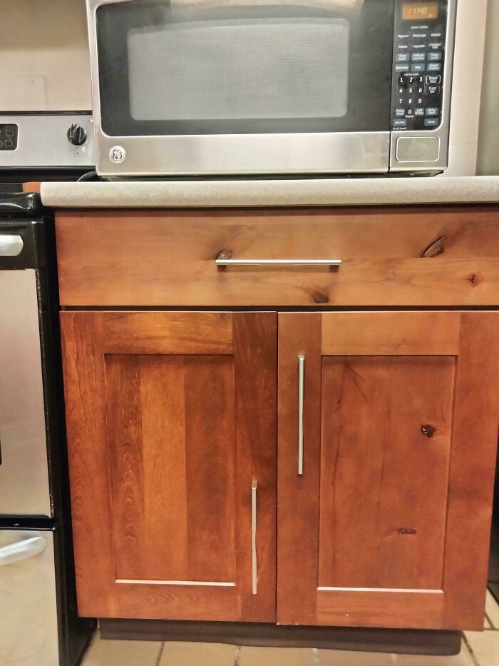 Kitchen cabinet fail with misaligned handles, next to a microwave.