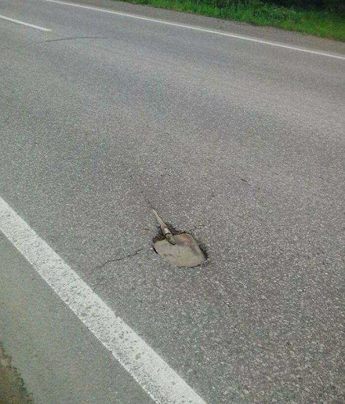 Road fail with a shovel buried in the pavement, illustrating a classic "you had one job" moment.