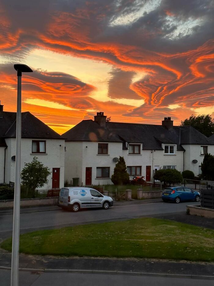 Dramatic orange and red sunset clouds over suburban houses, showcasing nature's beauty.