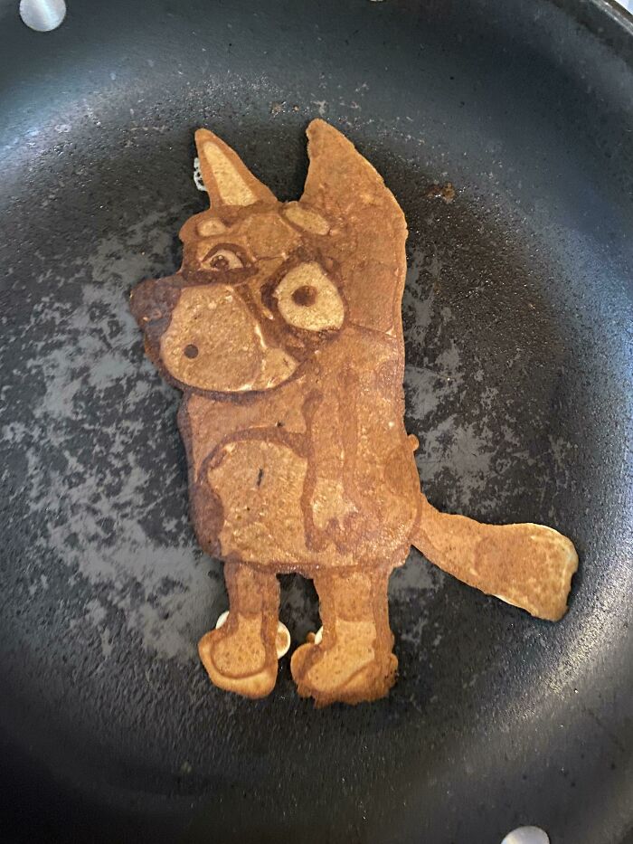 Pancake shaped like a cartoon dog cooking in a skillet, capturing a funny and goofy moment about being a dad.