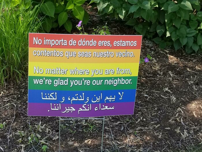 Wholesome multilingual yard sign about welcoming neighbors, set against greenery.
