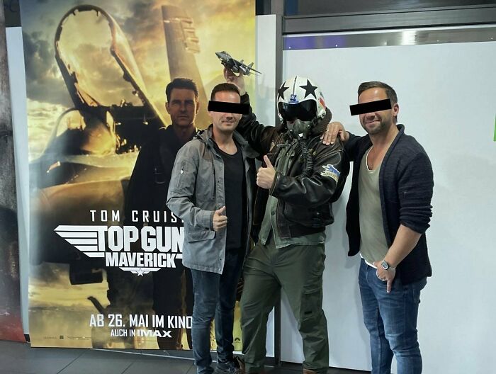 Three men posing with a Top Gun: Maverick poster, one in pilot gear, exemplifying system-cheating confidence.