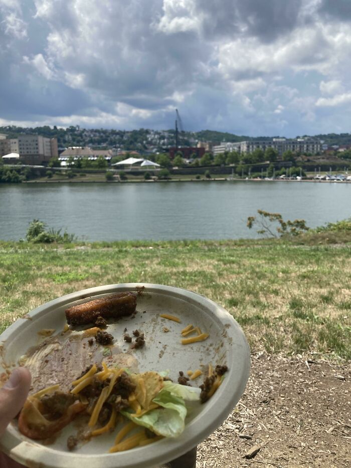 A paper plate with leftover food held by a river, person blending into the natural setting.