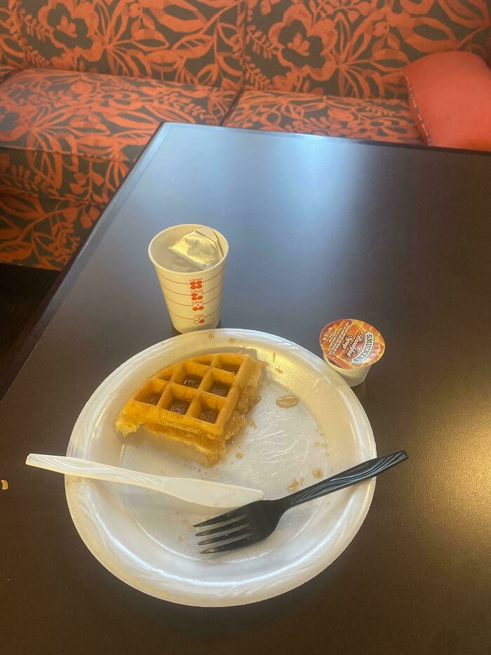 Waffle and syrup on a plate with a plastic fork, subtly cheating the system for a free breakfast setup.